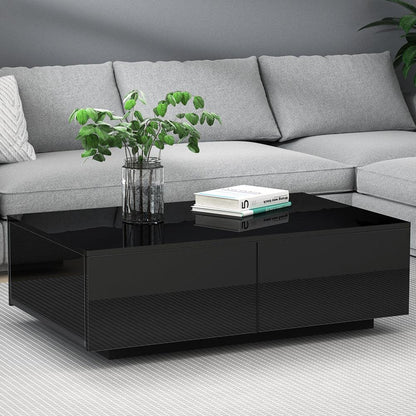 Modern black coffee table with glass top, books, and a plant, in front of a grey sofa.