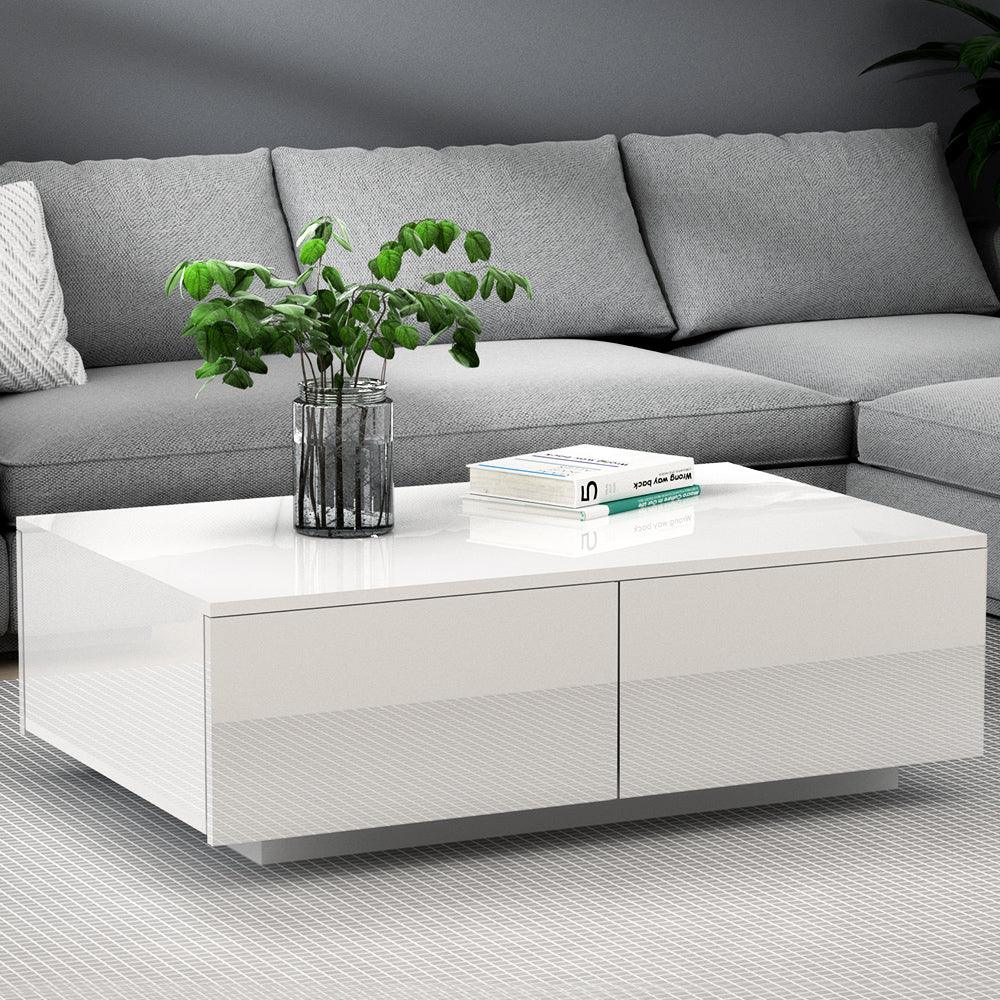 Modern white gloss coffee table with plant and books, in front of a grey sectional sofa
