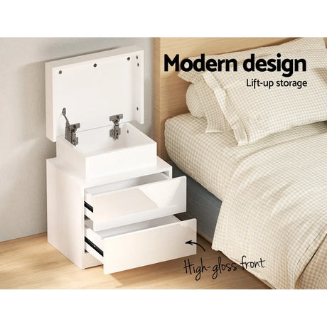 Modern white bedside table with lift-up storage, high-gloss front, next to bed.