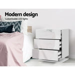 White modern LED bedside table with glossy drawers next to a bed, minimal bedroom decor