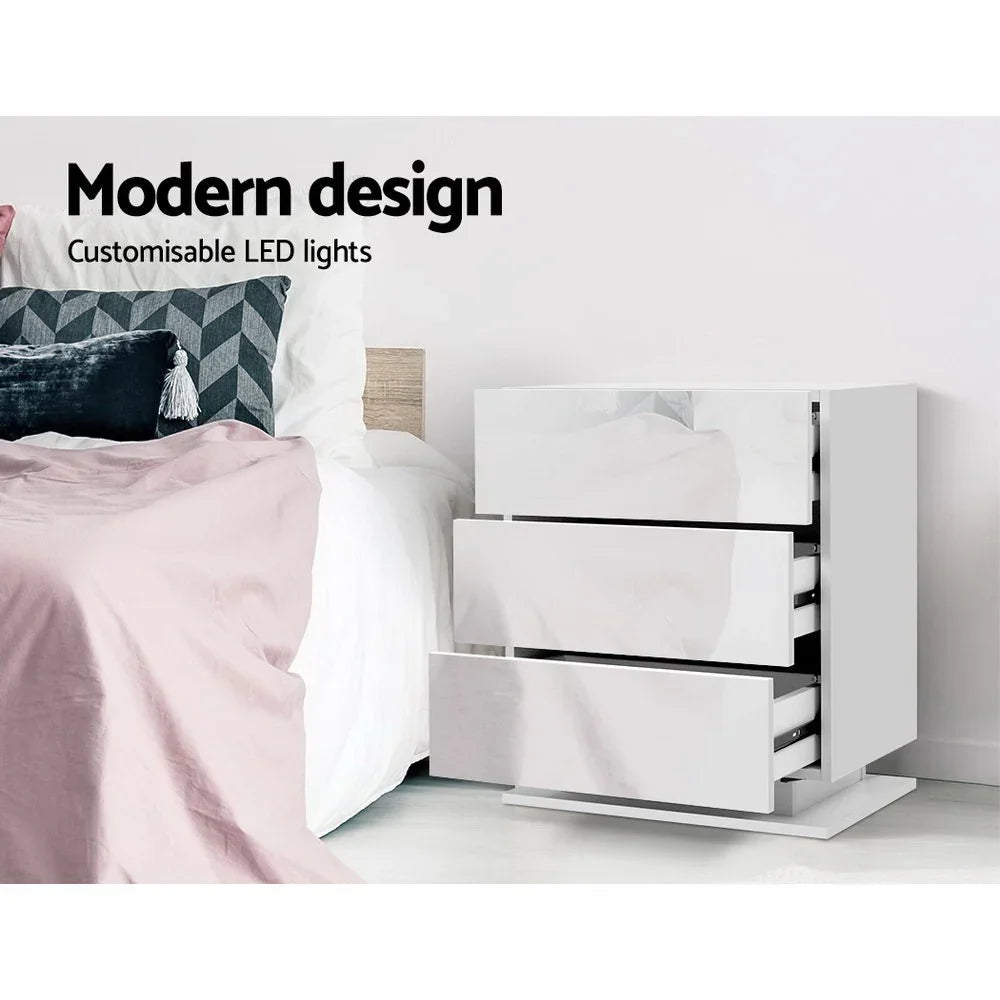 White modern LED bedside table with glossy drawers next to a bed, minimal bedroom decor