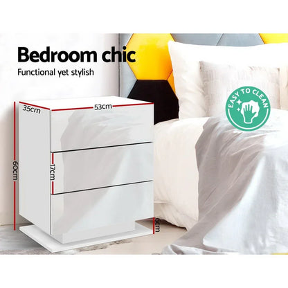 White modern three-drawer bedside table with dimensions, beside a bed in a chic bedroom