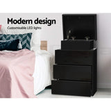Modern black bedside table with customizable LED lights and open drawers beside a bed