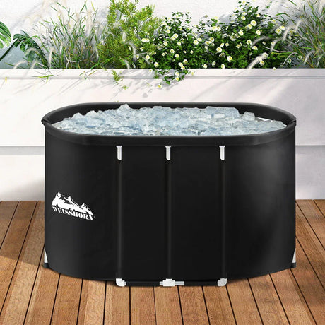 Weisshorn black ice bath tub filled with ice on wooden deck, outdoor plants behind