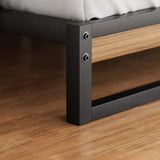 Close-up of black metal bed frame leg with wooden accent on wood floor
