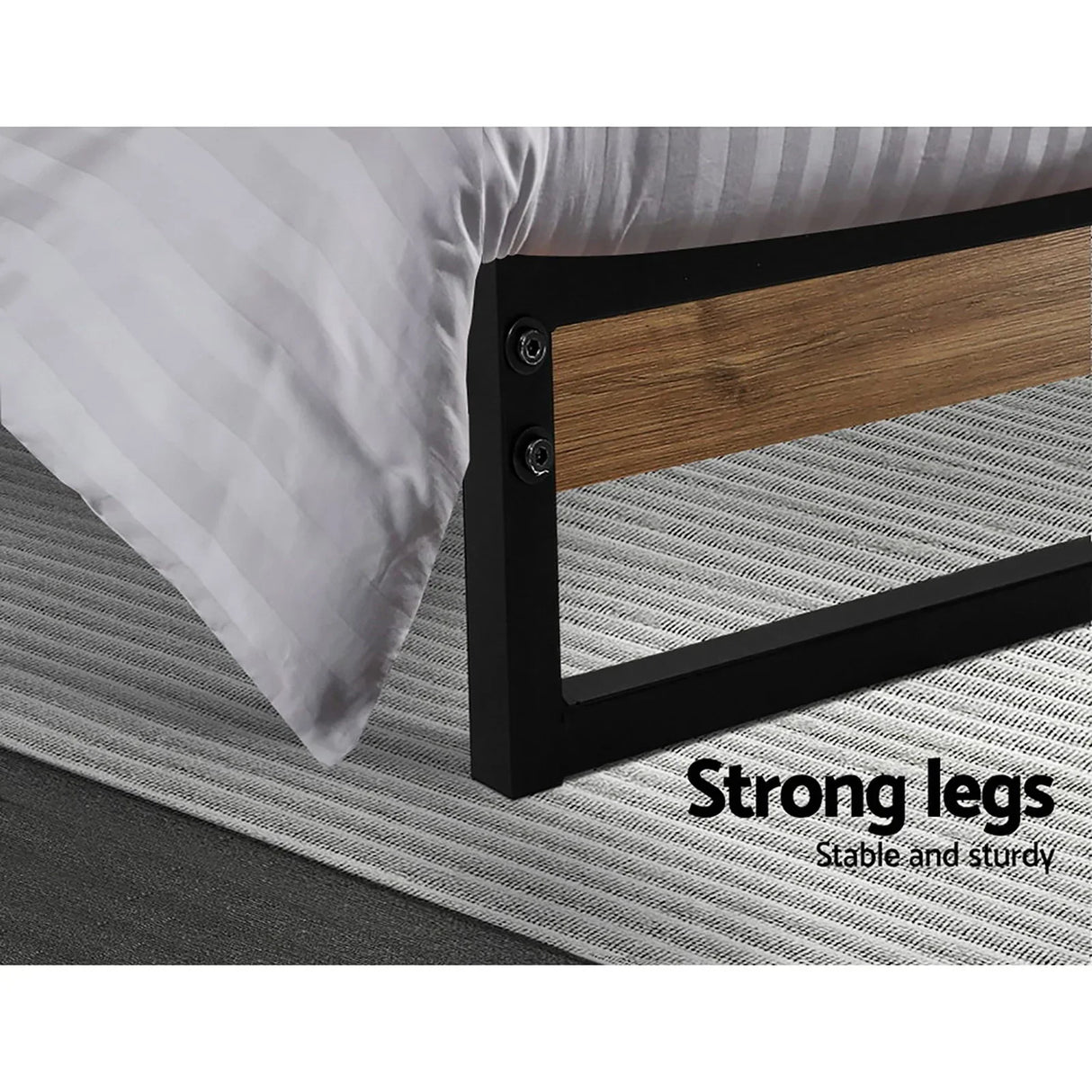 Close-up of bed frame leg with black metal and wood panel on gray striped rug, white bedding corner