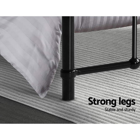 Black metal bed frame legs on gray textured rug with white striped bedding corner