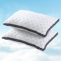 Two white pillows with quilted diamond pattern and black edges floating against a blue sky with clouds