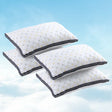 Set of four white quilted pillows with black edging floating against a blue sky with clouds
