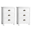 Pair of white three-drawer nightstands with brass cup handles on white background