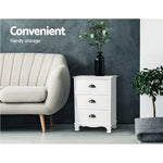 White three-drawer cabinet beside beige sofa, decorative vase on top, modern living room