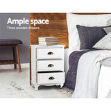 White wooden bedside table with three drawers in modern bedroom setting