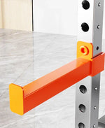 Orange steel rack attachment on metal gym squat rack, standing on gray marble floor