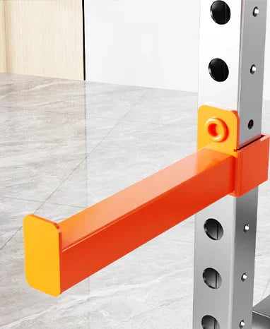 Orange steel rack attachment on metal gym squat rack, standing on gray marble floor