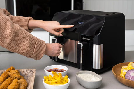 Person using a black Healthy Choice air fryer on kitchen counter with fried chicken, fries, and sauces