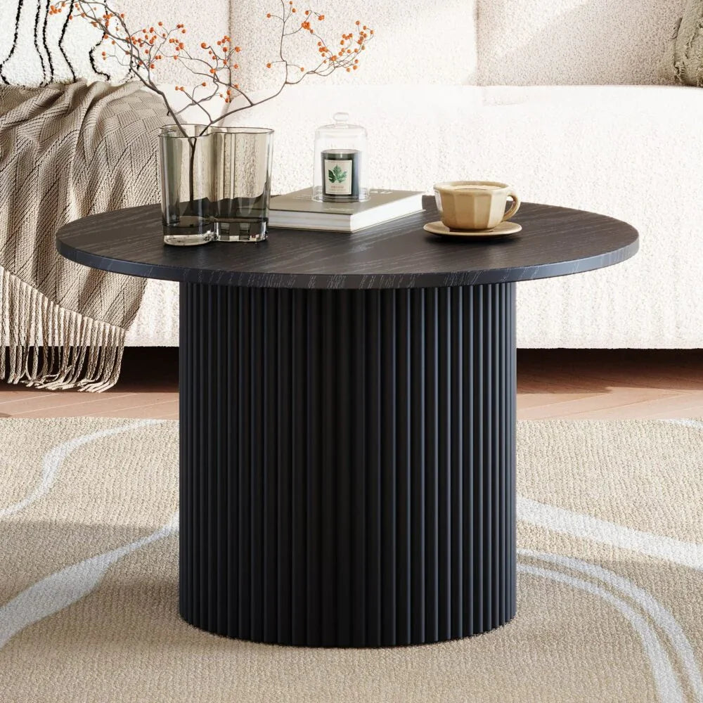 Modern black round coffee table with ribbed pedestal base, decor, and cozy living room setting