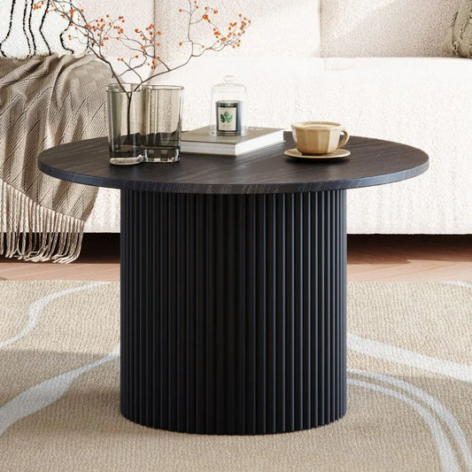 Modern black round coffee table with ribbed pedestal base, decor, and cozy living room setting
