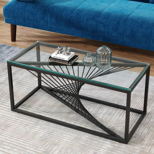 Modern glass coffee table with black metal geometric base in living room, blue sofa in background
