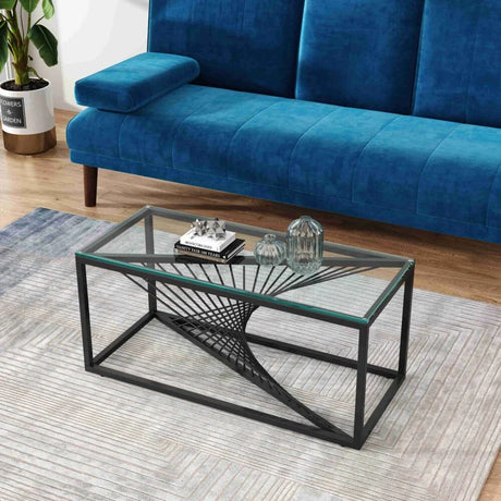 Modern glass coffee table with geometric black metal base in front of a blue velvet sofa