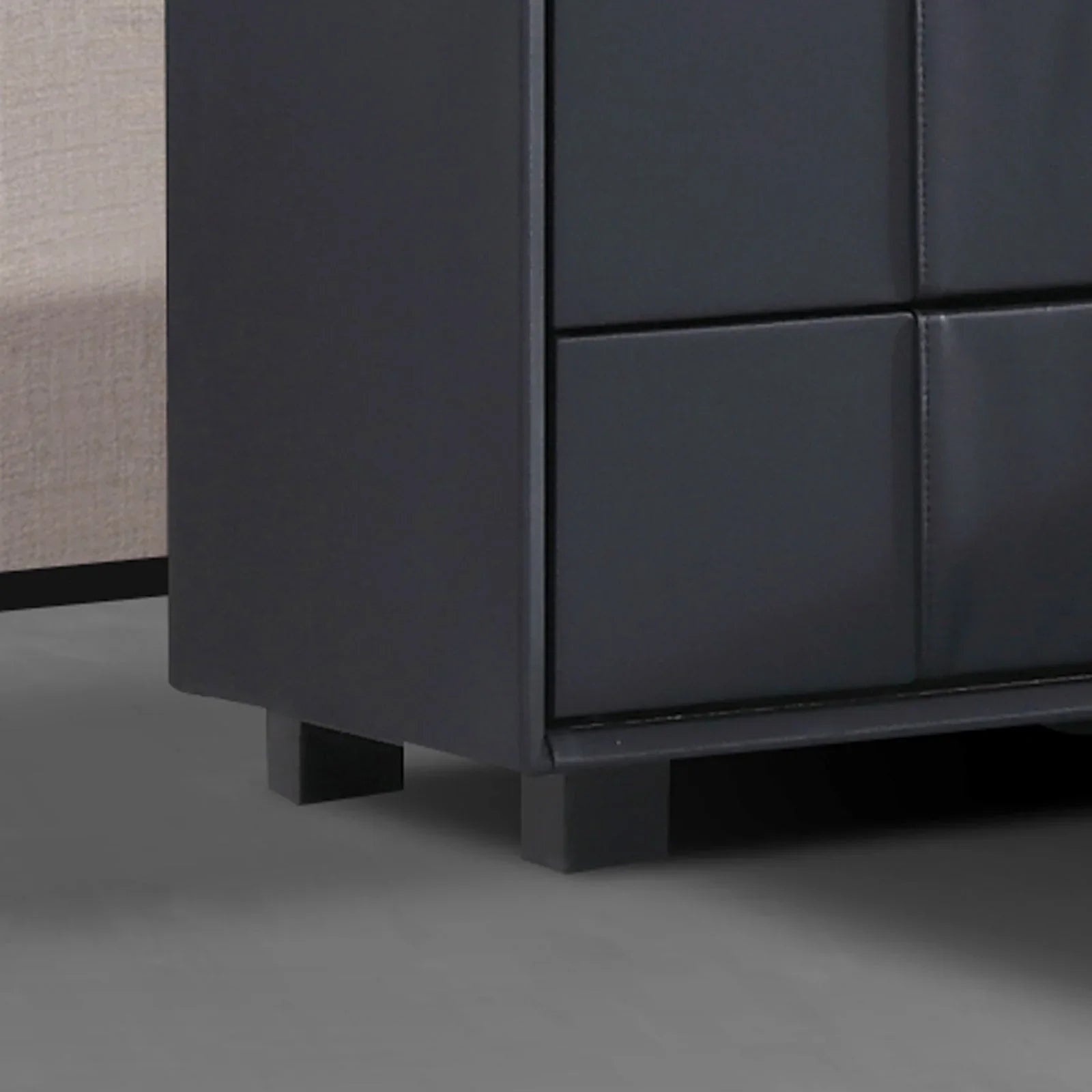 Black faux leather dresser corner with square padded drawer fronts on gray floor