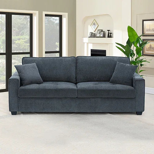 Modern dark gray sofa with two pillows in a bright living room with fireplace and plant