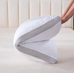 Hand folding a white pillow with gray mesh breathable sides on a beige bed