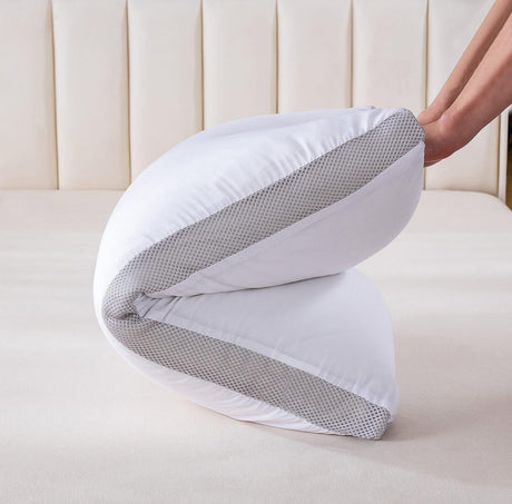 Hand folding a white pillow with gray mesh breathable sides on a beige bed