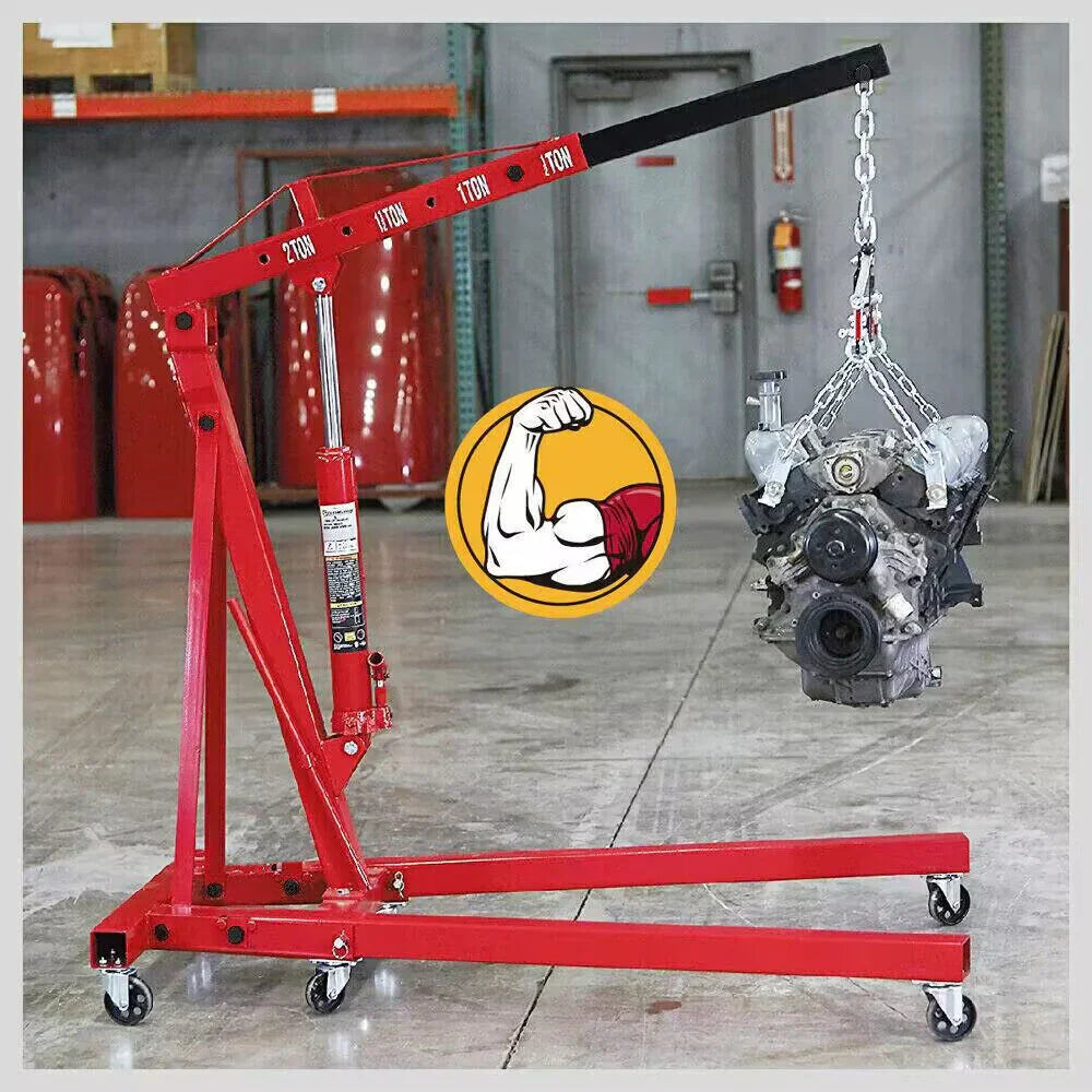 Red 2-ton hydraulic engine hoist lifting a car engine in a workshop with concrete floor