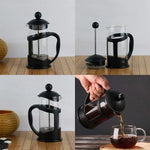Black French press coffee maker on wooden board, with assembly parts and pouring brewed coffee