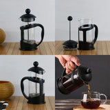 Black French press coffee maker on wooden board, with assembly parts and pouring brewed coffee