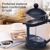Black French press coffee maker with glass carafe on table, white cup, coffee beans, and cozy kitchen background