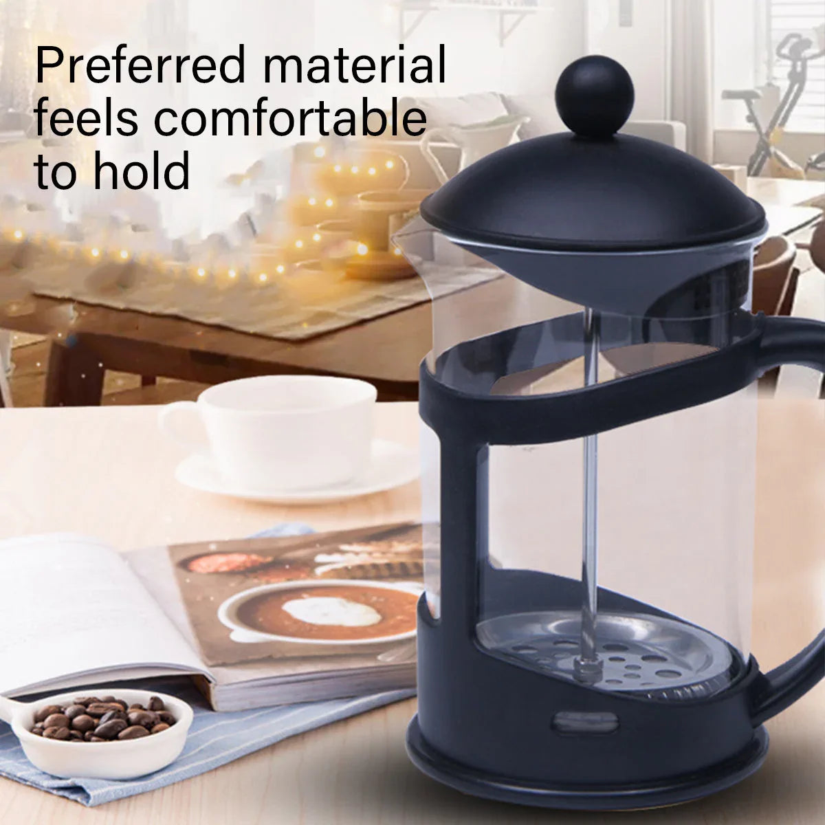 Black French press coffee maker with glass carafe on table, white cup, coffee beans, and cozy kitchen background