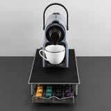 Compact grey coffee pod machine with white cup on top and colorful pods stored in drawer below