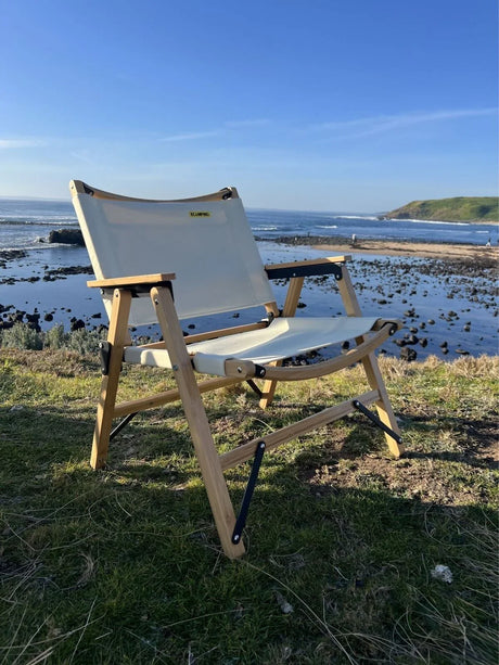 White fabric and wood camping chair on grassy cliff overlooking rocky ocean shoreline and clear blue sky