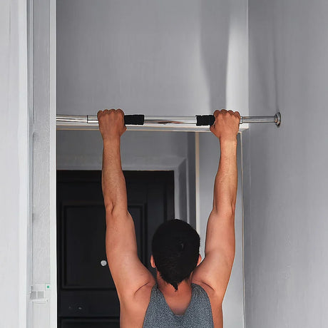Man doing pull-up exercise on a metal doorway pull-up bar in a home setting