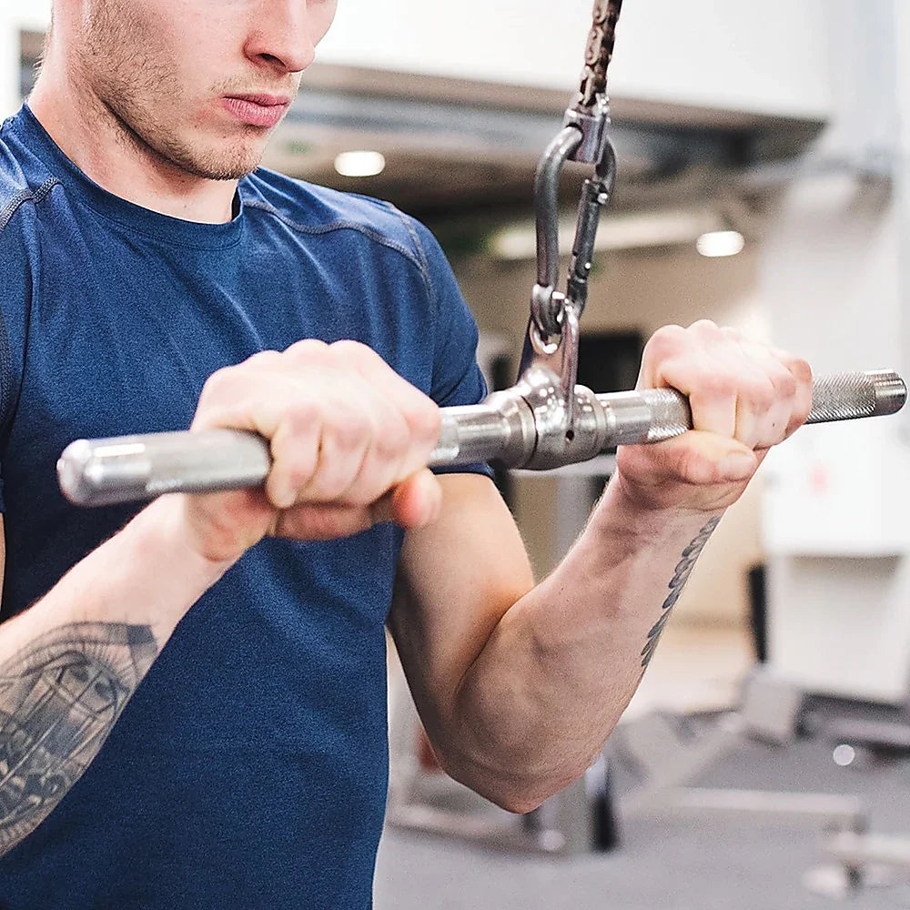 Close-up of man in blue shirt gripping metal handle on gym cable machine for strength training