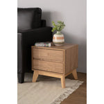 Modern wooden nightstand with two drawers, books, and a vase with greenery beside black sofa