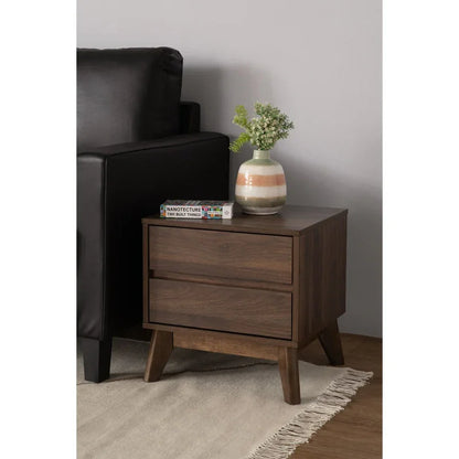 Mid-century modern walnut nightstand with books, vase, and plant beside black sofa