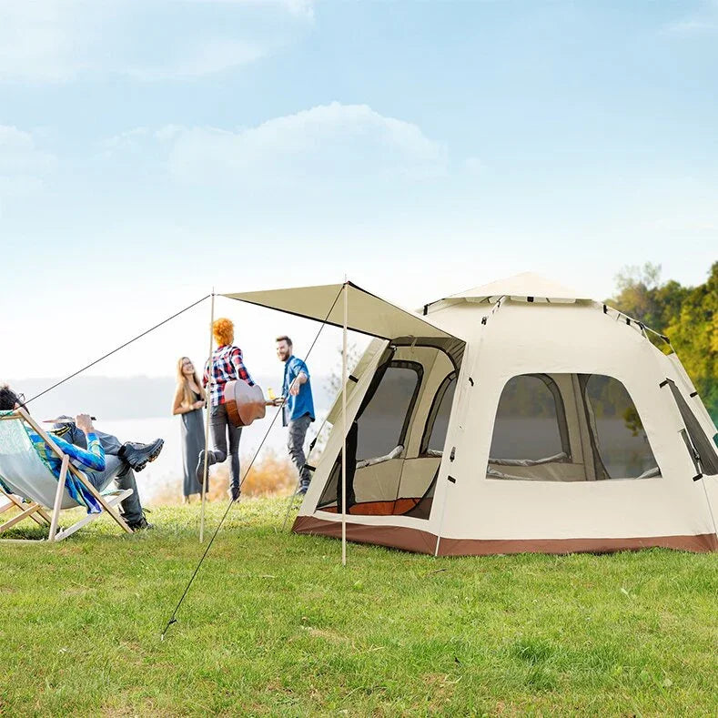 Group of friends camping outdoors with large beige tent and canopy on green grass under blue sky