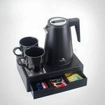 Black electric kettle with two black mugs on tray with drawer holding coffee and tea packets
