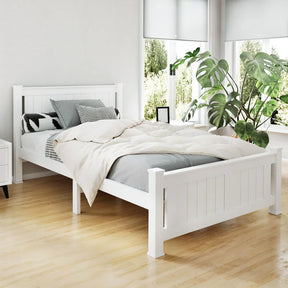 White wooden bed with gray bedding and decorative pillows in bright room with large windows and green plant