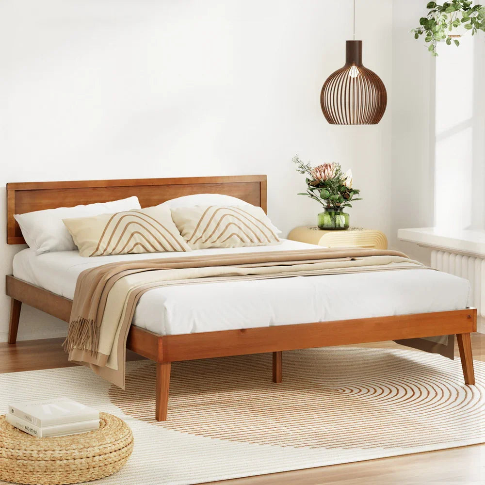 Modern wooden bed with beige and white bedding in bright minimalist bedroom, rattan stool and pendant lamp