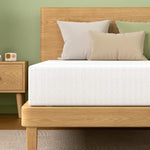 Modern wooden bed frame with white mattress and three pillows in neutral and green tones, next to wooden nightstand
