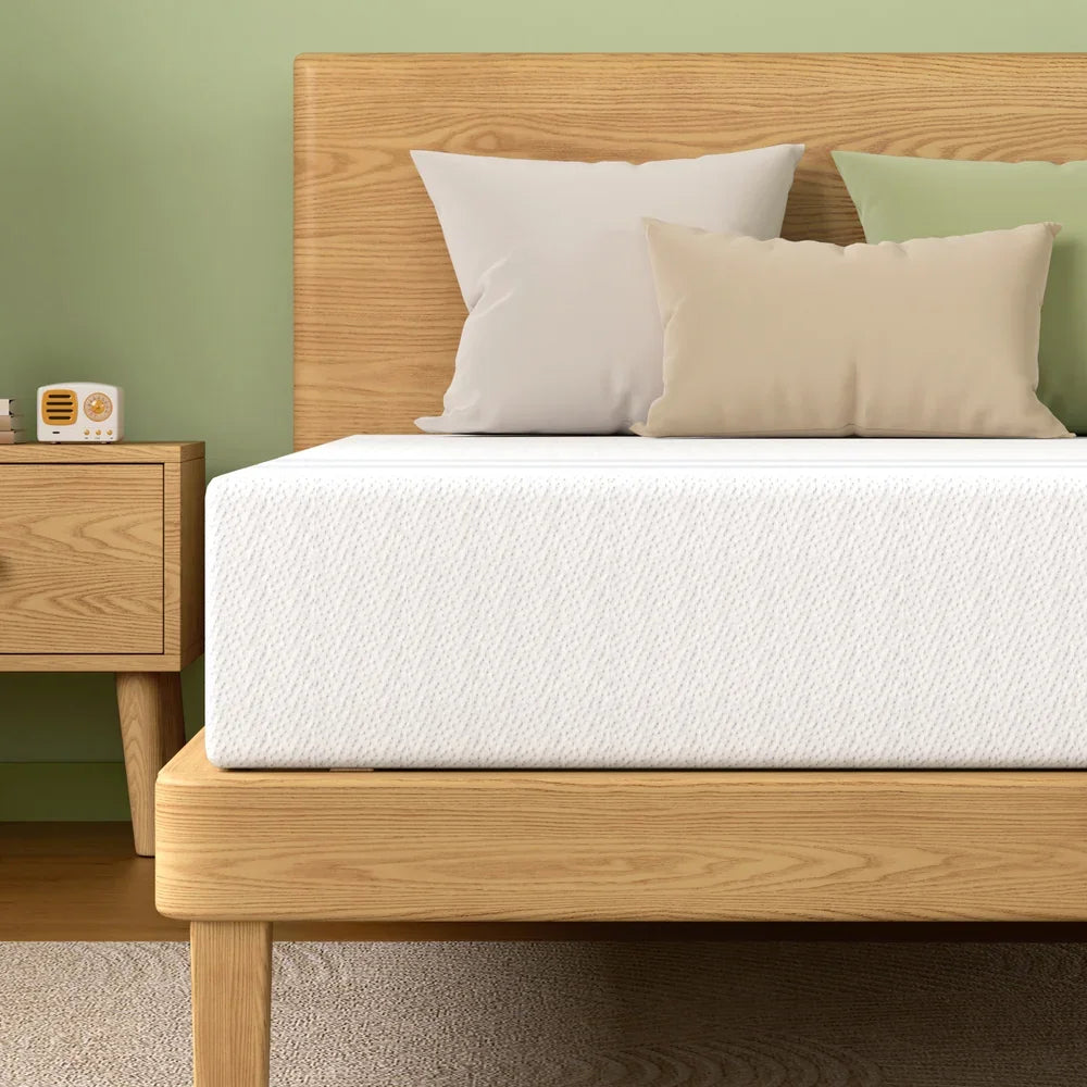White mattress on wooden bed frame with beige and white pillows, green wall, wooden nightstand with retro radio